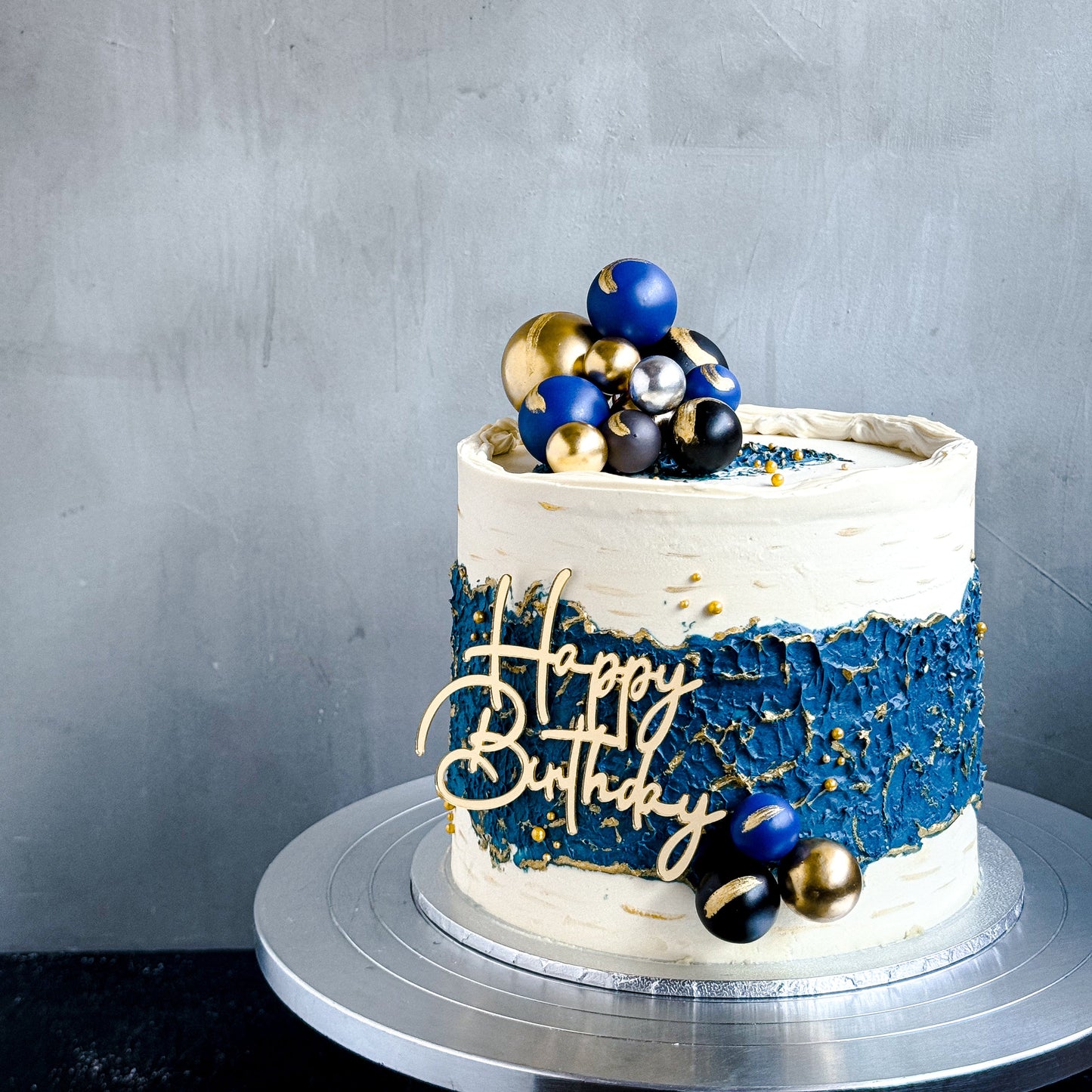 Elegant bespoke cake from Kaki Desserts, decorated with intricate icing and colorful floral accents on a white cake stand.