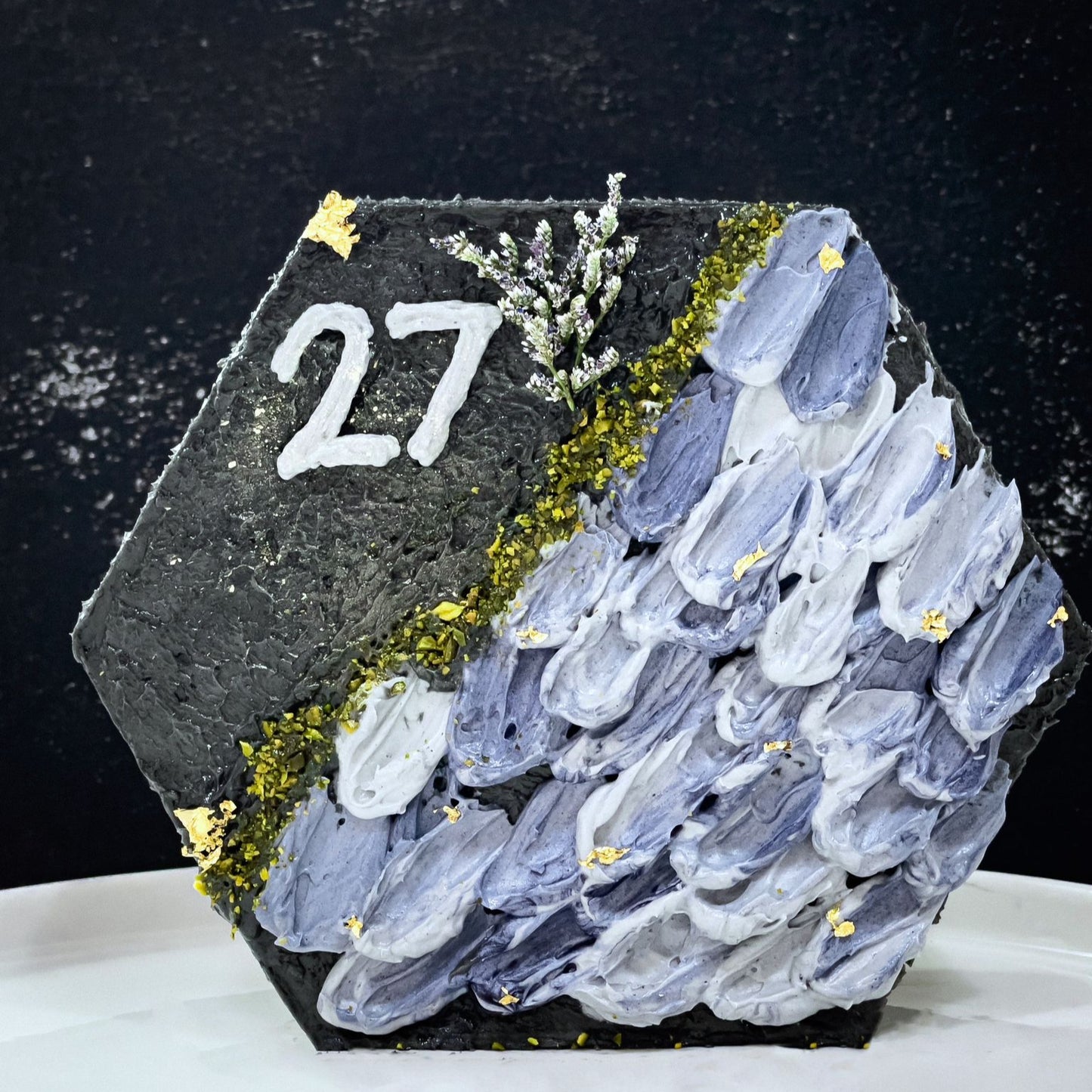 Decorative bespoke cake from Kaki Desserts with intricate icing designs and colorful floral accents, displayed on a white cake stand.