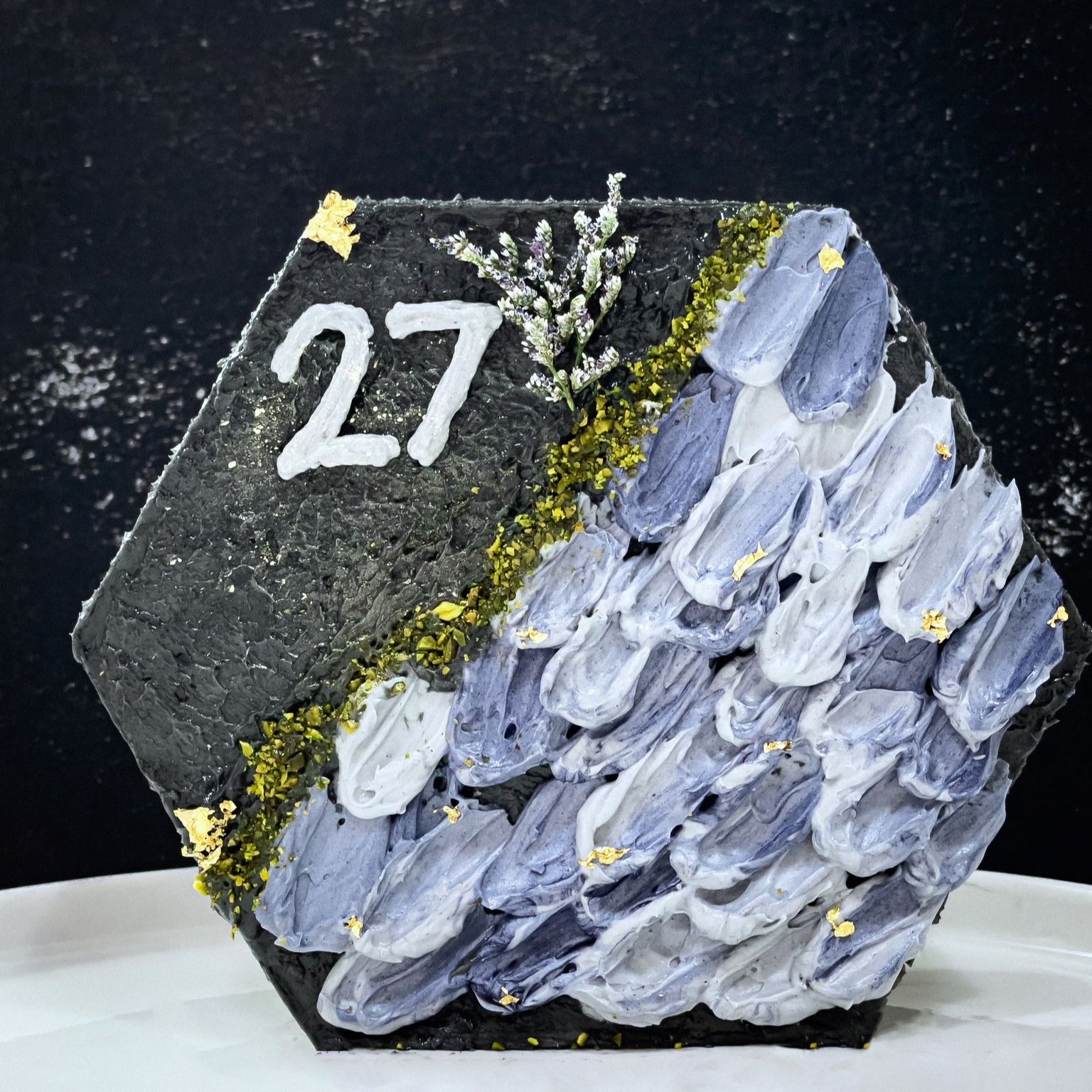 Decorative bespoke cake from Kaki Desserts with intricate icing designs and colorful floral accents, displayed on a white cake stand.