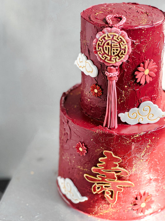 Two layered tier cakes from Kaki Desserts with white icing and decorative fruit toppings on a cake stand.