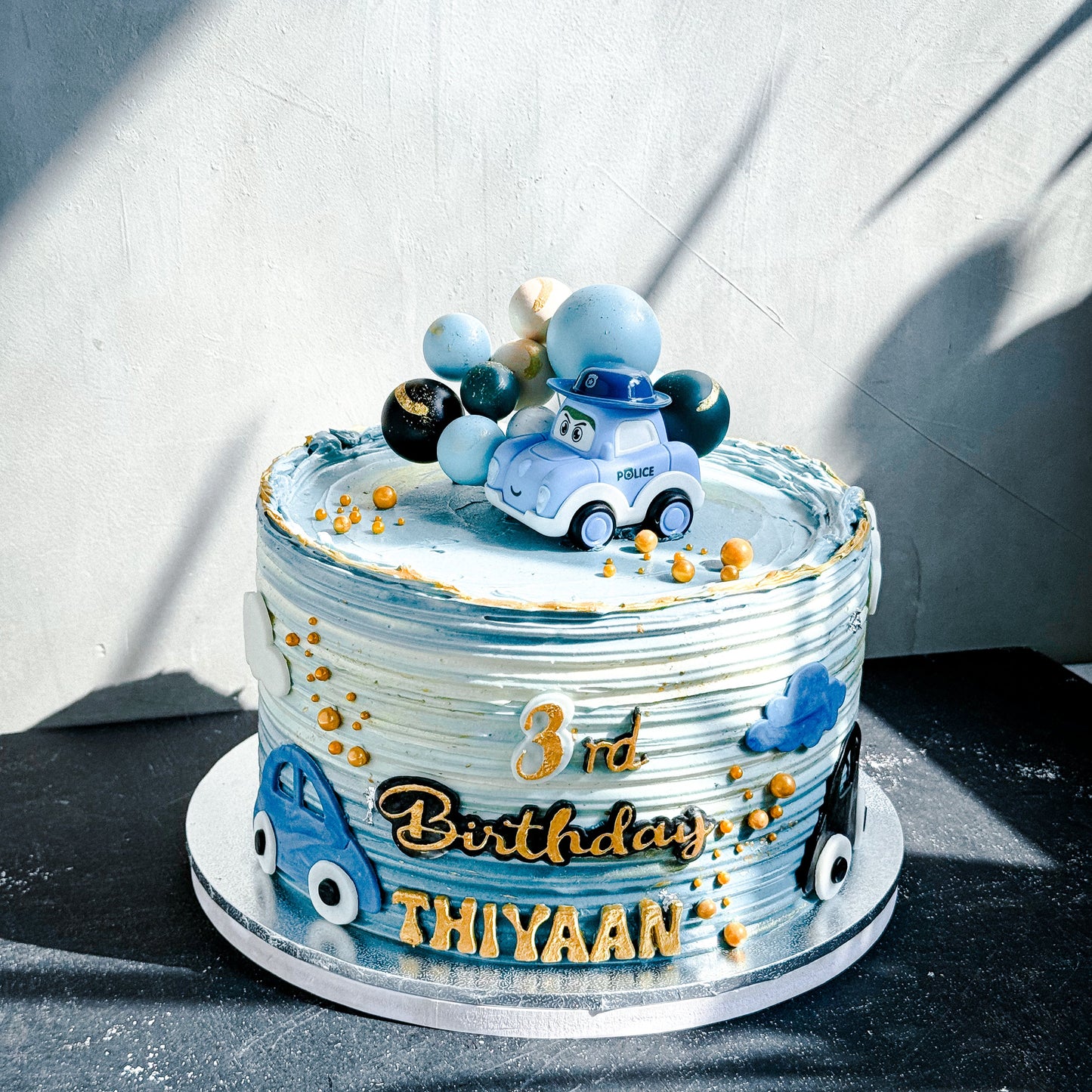 Decorative bespoke cake from Kaki Desserts with intricate icing details and elegant floral accents on a white cake stand.