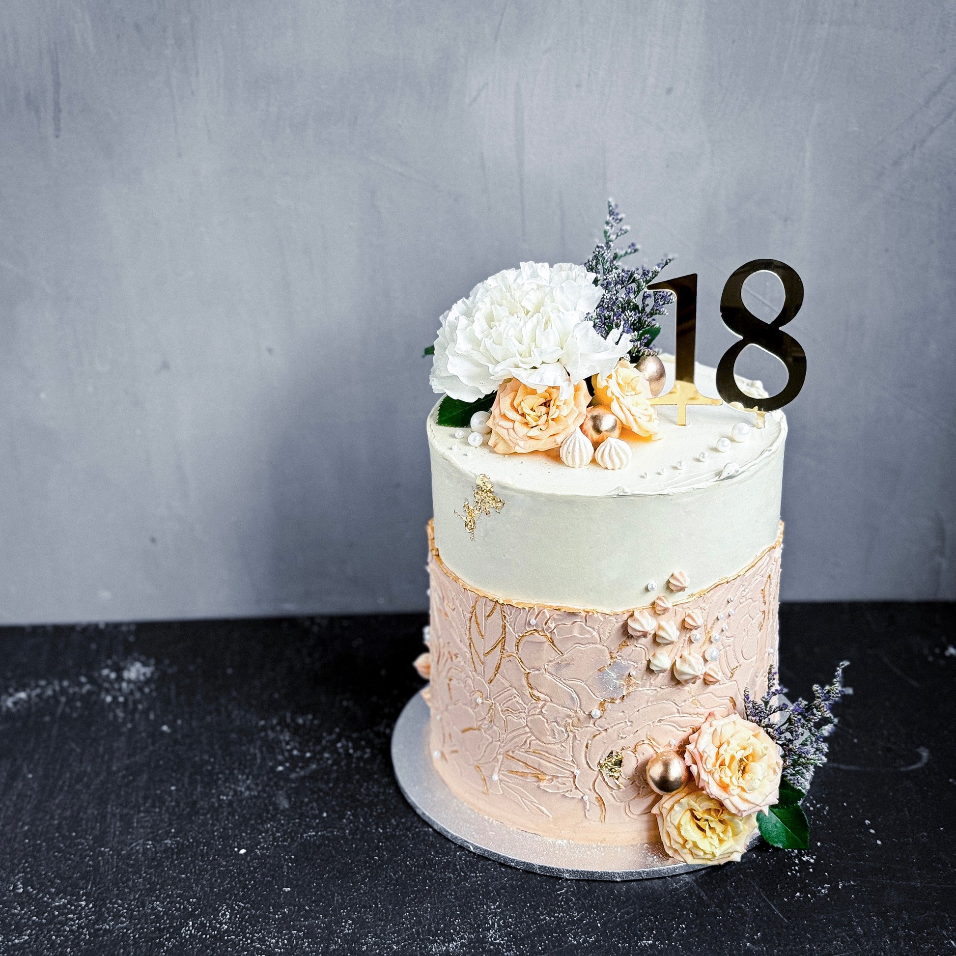 Decorative bespoke cake from Kaki Desserts with intricate icing details and colorful floral accents.