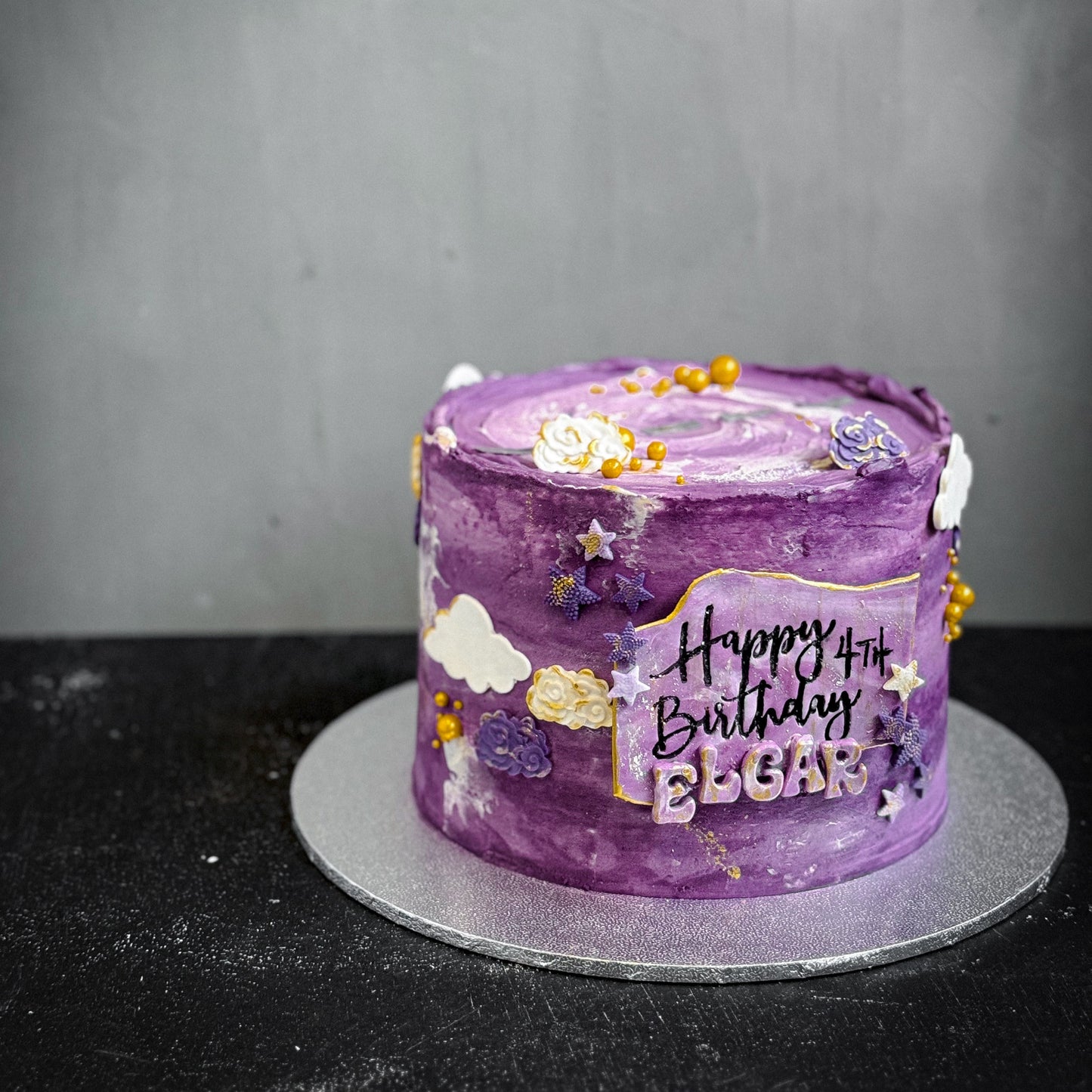 Assorted bespoke cakes from Kaki Desserts with elegant frosting and decorative toppings, displayed on a wooden table.