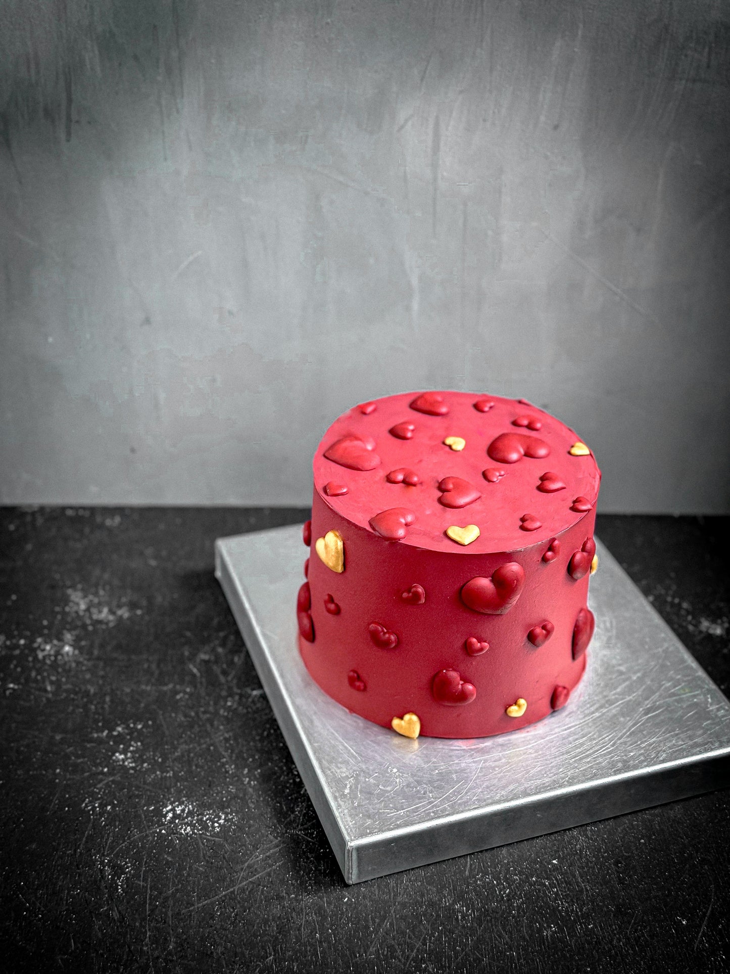 Decorative bespoke cake from Kaki Desserts featuring elegant floral icing and intricate piping, displayed on a white cake stand.