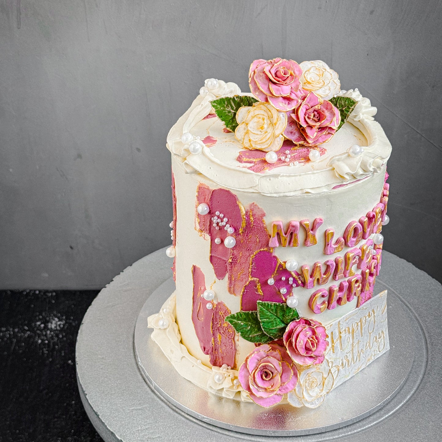 Decorative bespoke cake from Kaki Desserts with colorful floral icing and intricate piping, displayed on a white cake stand.
