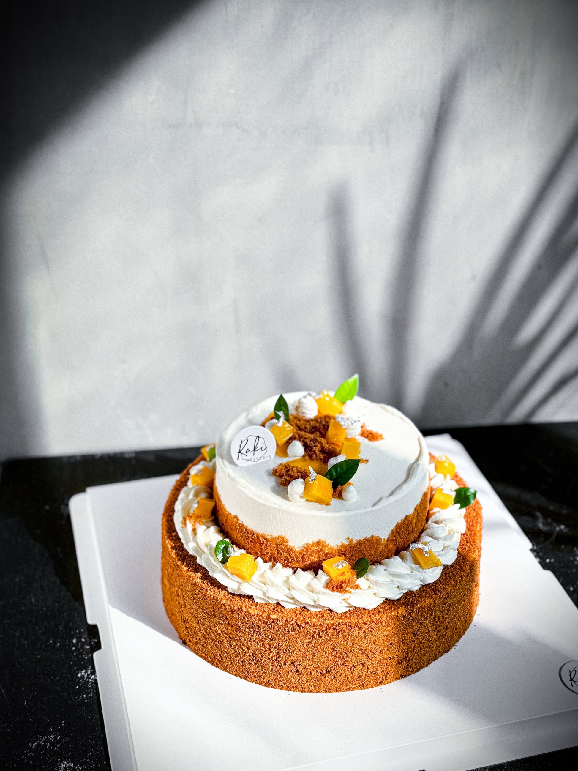 Elegant tier cake from Kaki Desserts with white frosting and decorative flowers, perfect for special occasions.