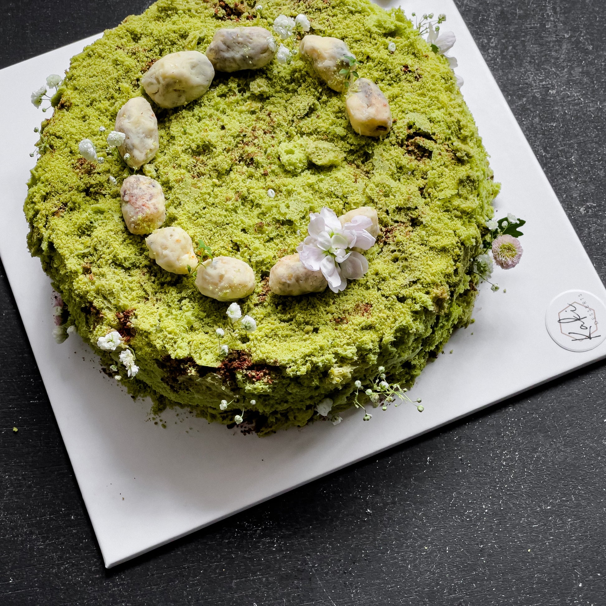 Decorative bespoke cake from Kaki Desserts with intricate floral and gold accents on a white frosting background.