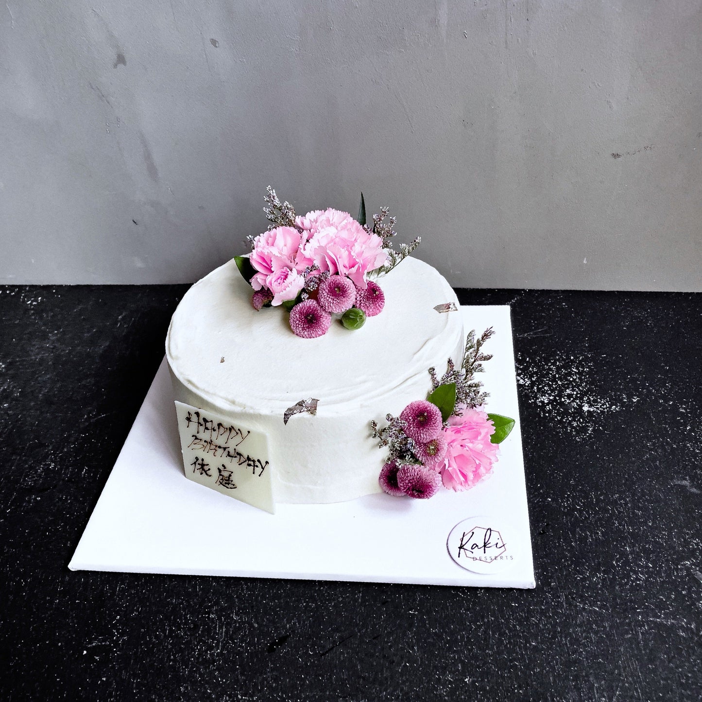 Decorative bespoke cake from Kaki Desserts featuring intricate icing designs and colorful floral accents.
