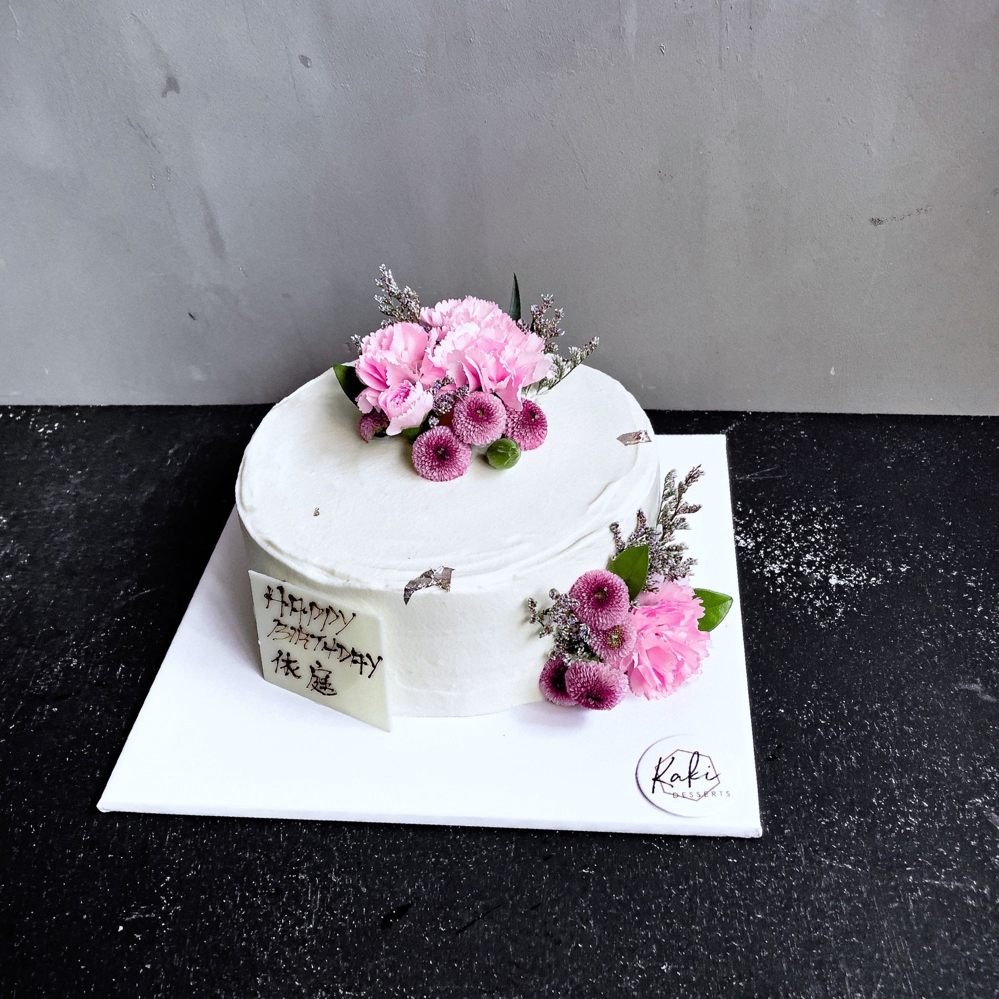 Decorative bespoke cake from Kaki Desserts featuring intricate icing designs and colorful floral accents.