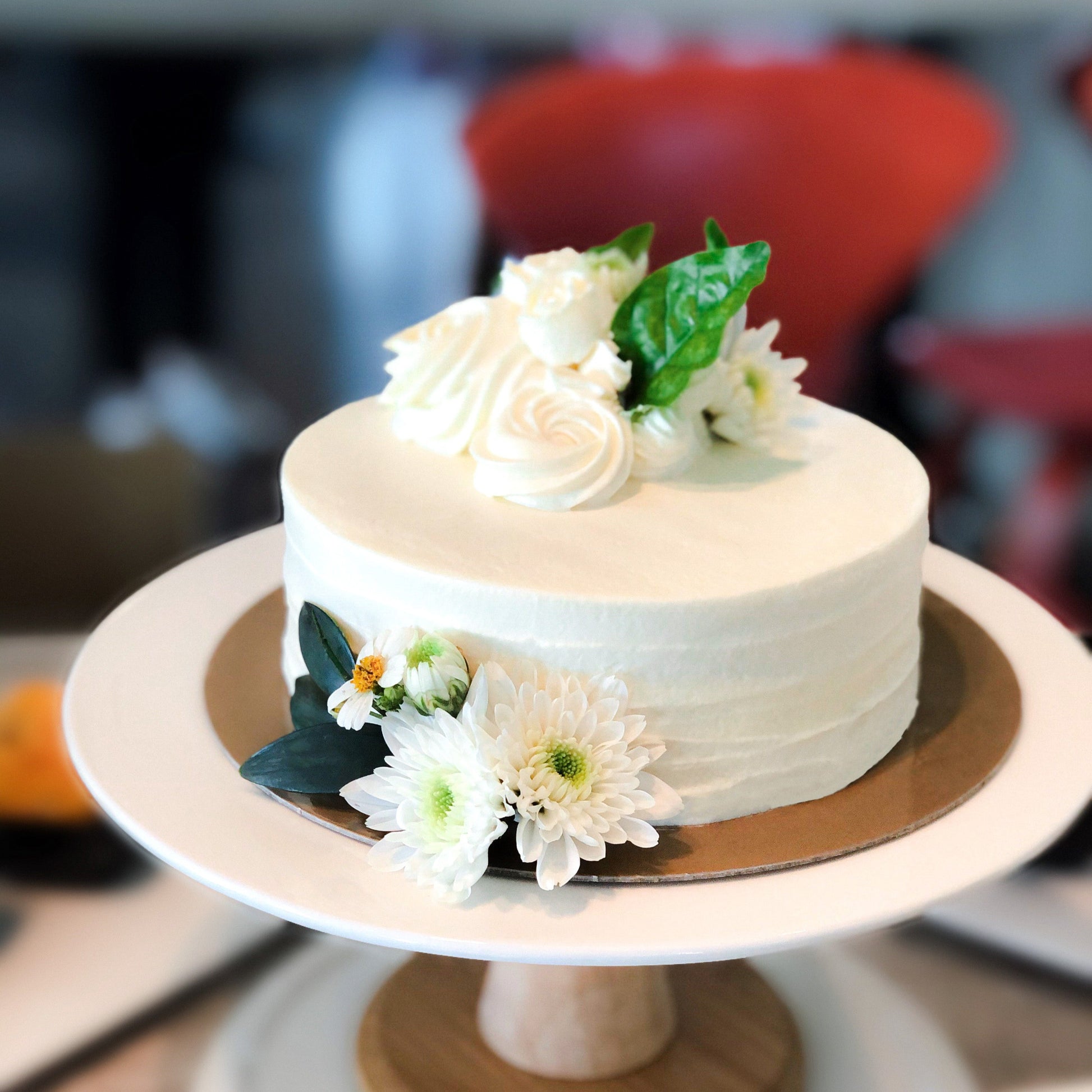 Decorative bespoke cake from Kaki Desserts featuring intricate icing designs and colorful floral accents.