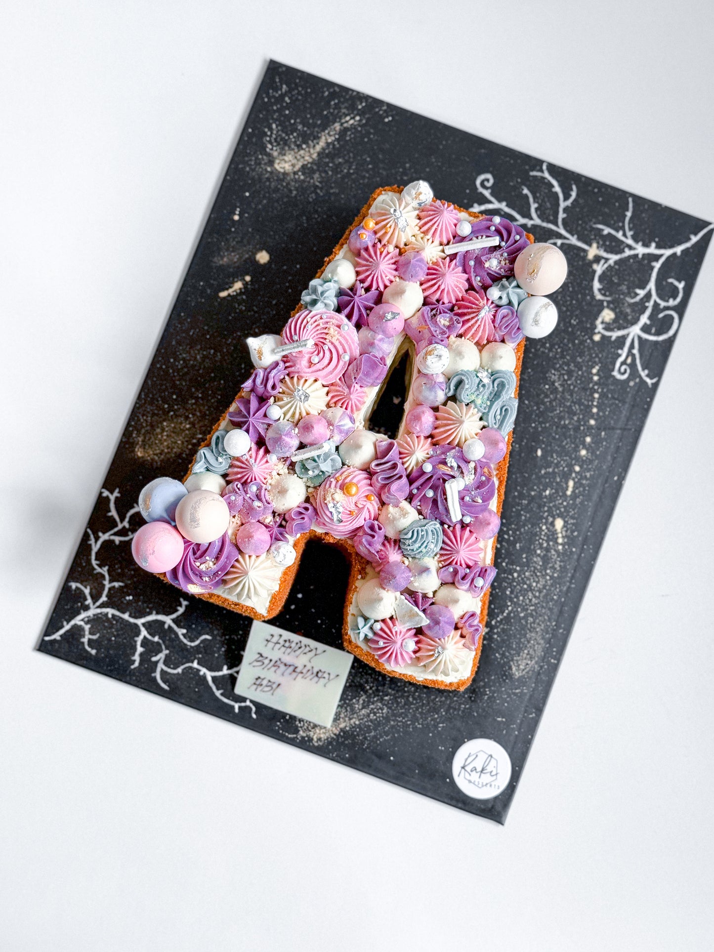 Letter cakes from Kaki Desserts featuring colorful, decorated cake slices arranged in letter shapes on a white background.