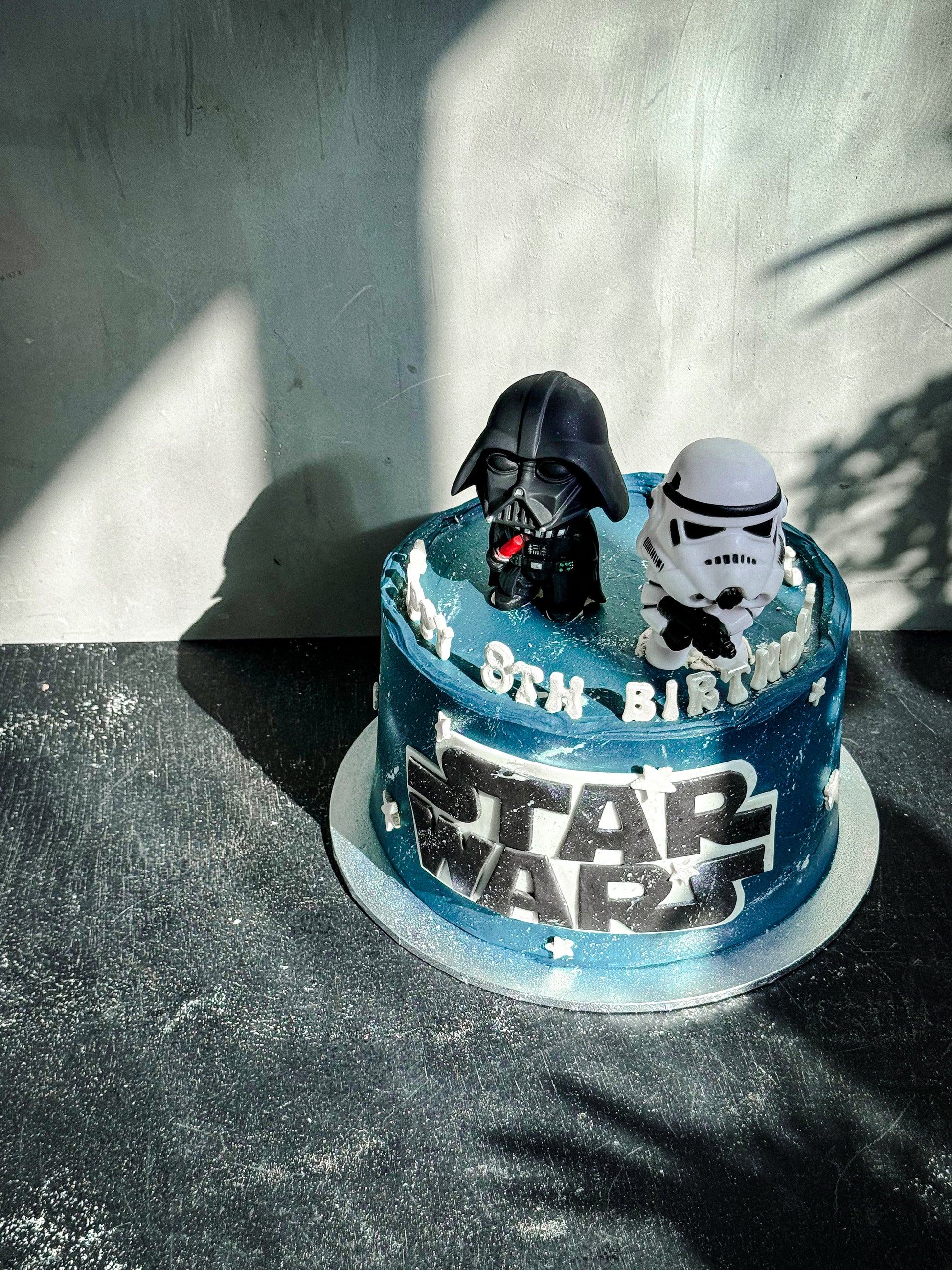 Close-up of a bespoke cake from Kaki Desserts, featuring elegant icing and decorative floral accents on a white cake stand.
