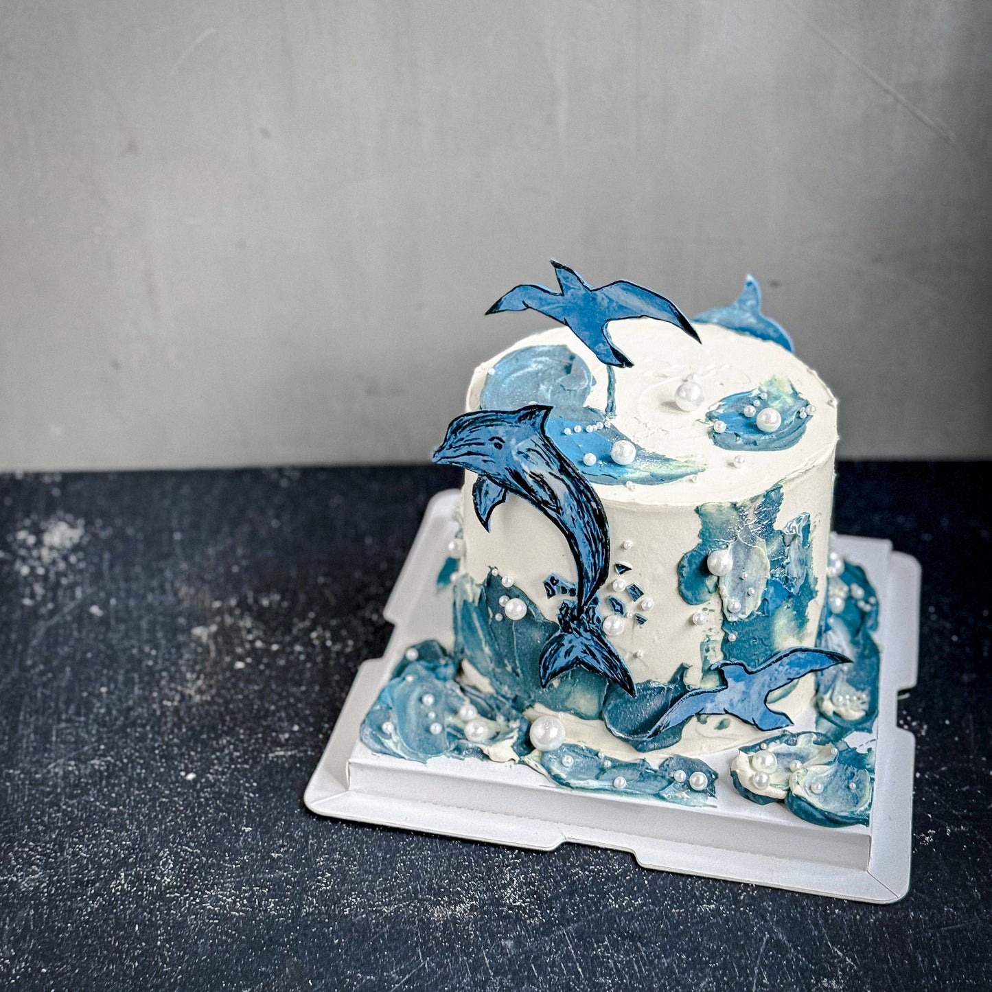 Decorative bespoke cake from Kaki Desserts featuring intricate icing details and elegant design on a white cake stand.