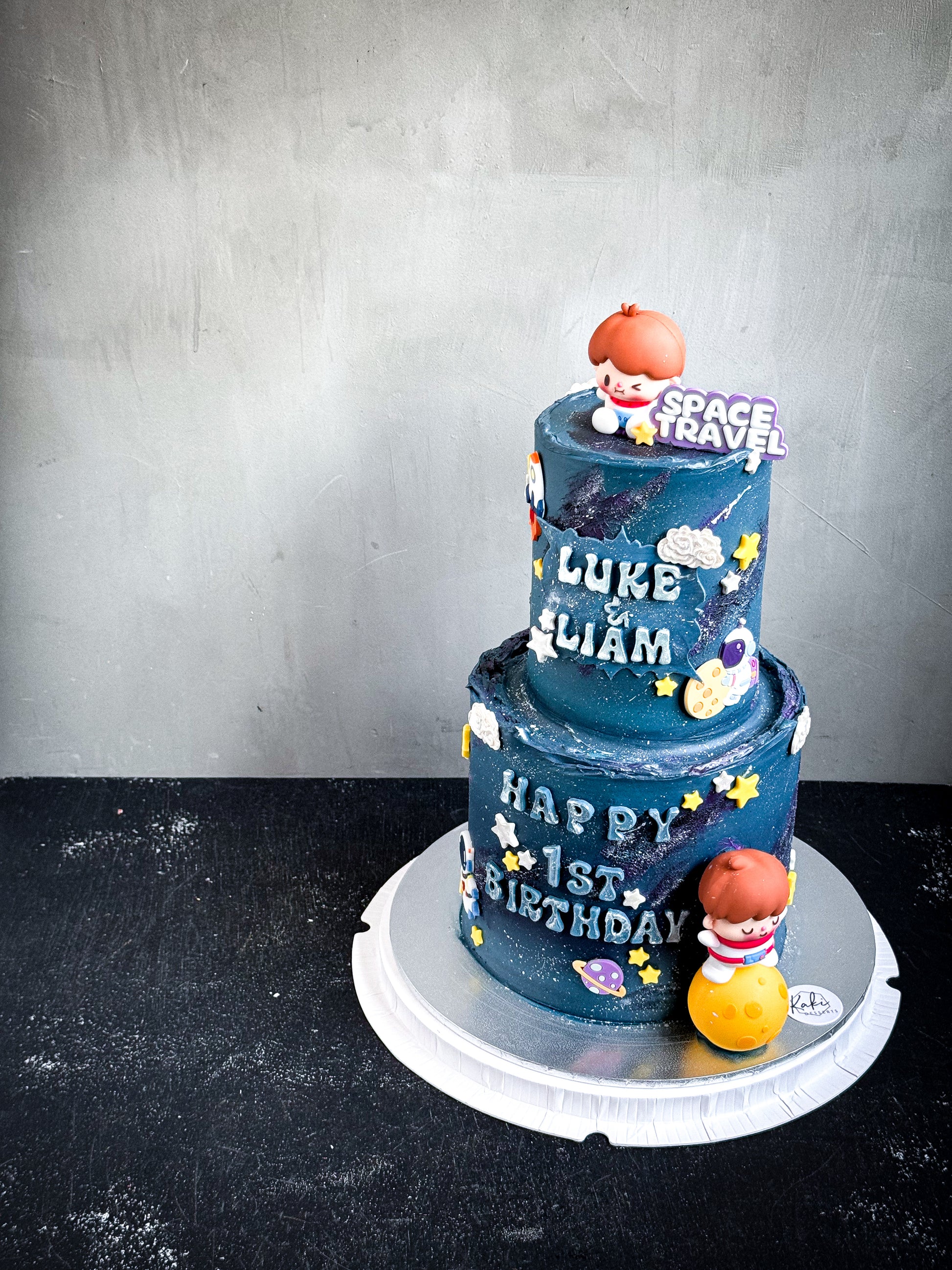 Assorted tier cakes from Kaki Desserts with elegant frosting and decorative toppings, displayed on a serving stand.