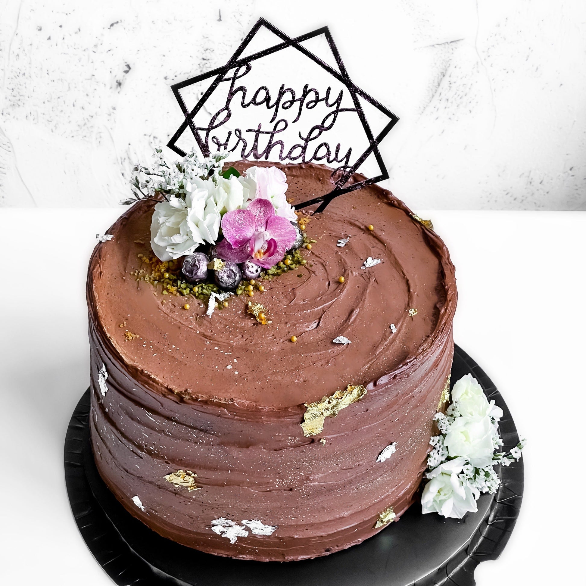 Bespoke cakes from Kaki Desserts featuring detailed, colorful icing and decorative toppings on a white platter.