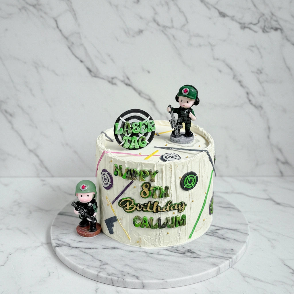 Marble laser tag themed cake from Kaki Desserts featuring detailed laser gun and game design in vibrant colors.