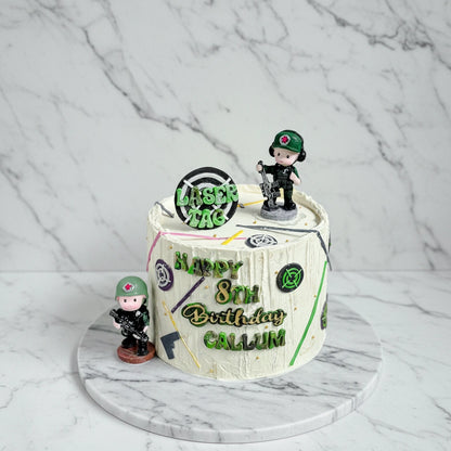 Marble laser tag themed cake from Kaki Desserts featuring detailed laser gun and game design in vibrant colors.