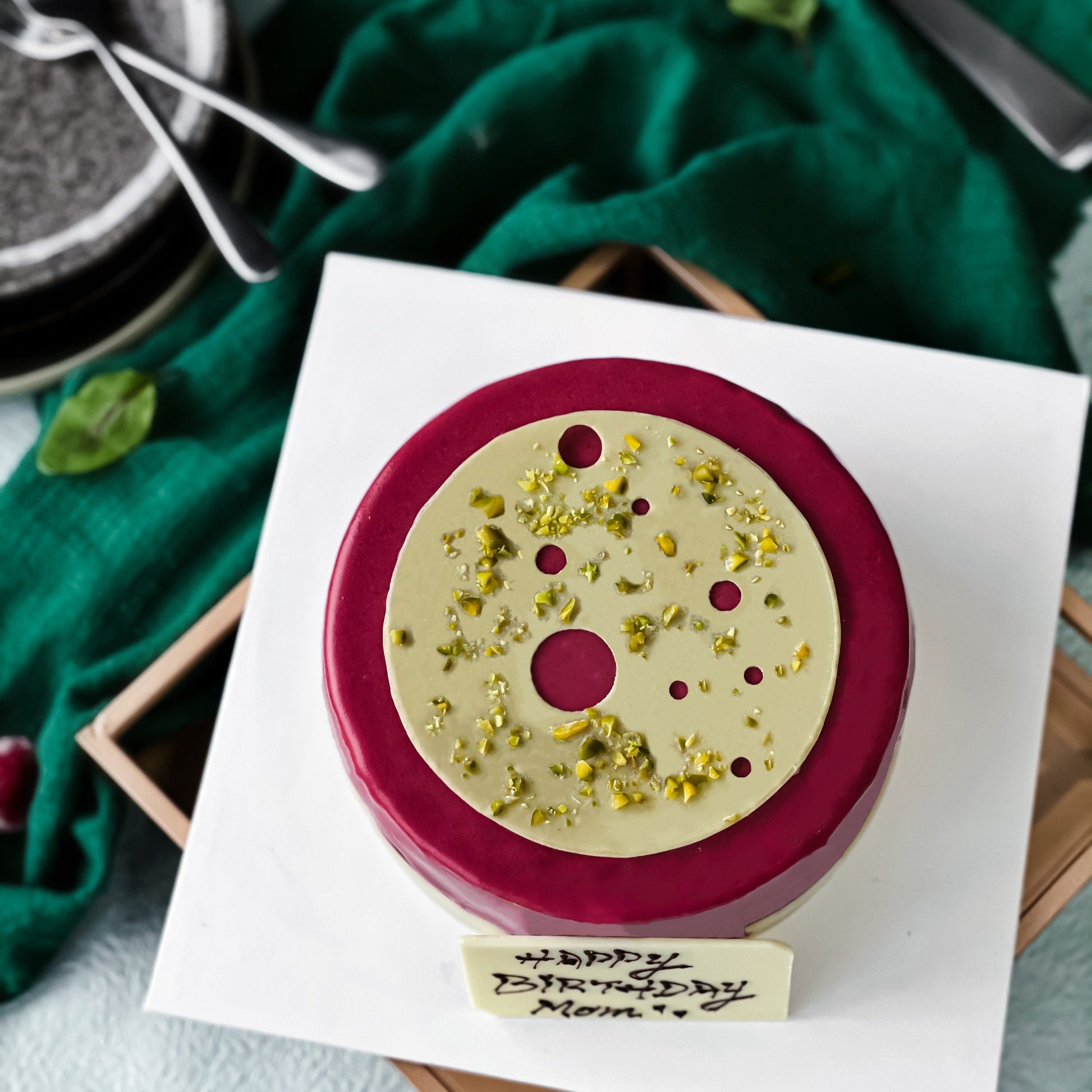 Kaki Desserts pistachio raspberry cake with layered green pistachio and pink raspberry frosting, topped with fresh raspberries and pistachios.